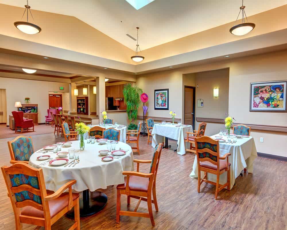 A well-lit dining room with neatly arranged tables and chairs, featuring floral decorations and modern decor.