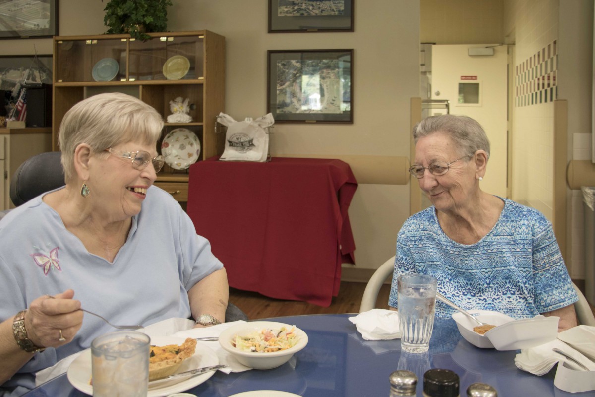 Two elderly women enjoying a meal together and sharing a laugh.