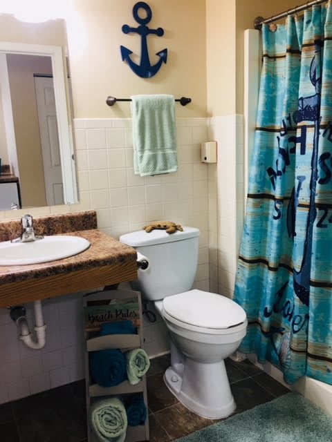 A nautical-themed bathroom with an anchor decoration, featuring a toilet, sink, and a shower curtain.