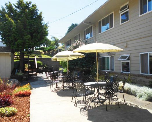A sunny outdoor patio area with tables, chairs, and umbrellas next to a building.