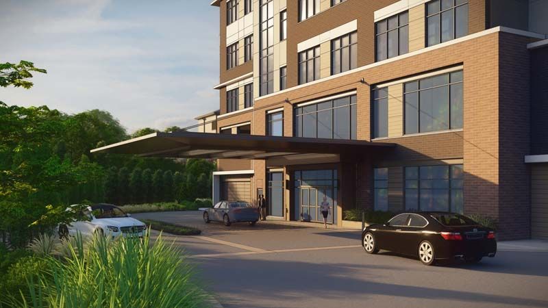 A modern building entrance with cars parked in the driveway.