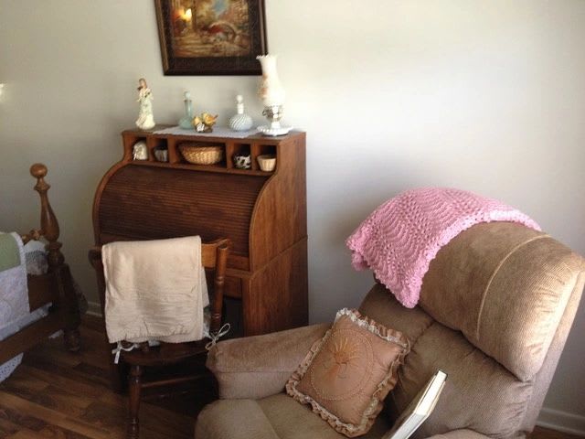 A cozy living room corner featuring a recliner with a pink throw, a wooden secretary desk adorned with decorative items, and a rocking chair.