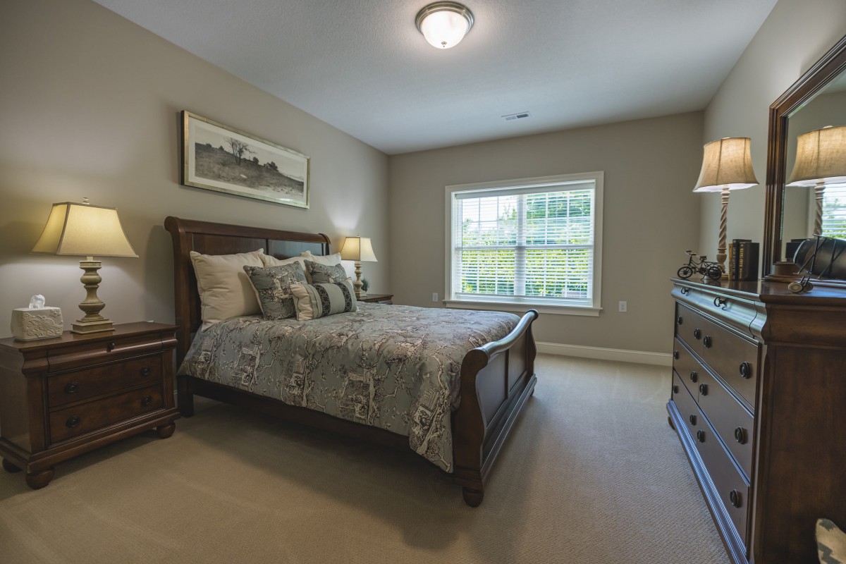 A cozy bedroom featuring a neatly made bed, wooden furniture, and natural light streaming through the window.