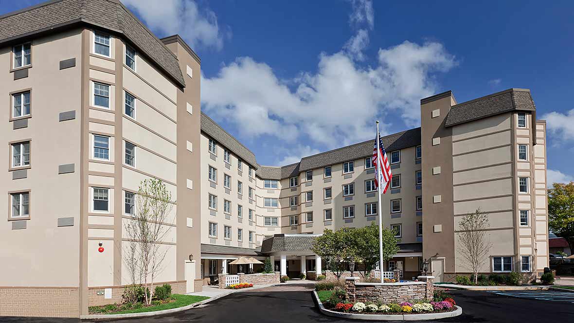 A modern hotel building with an American flag displayed at the entrance on a partly cloudy day.