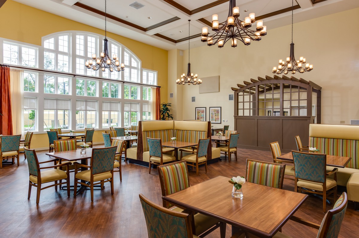 A well-lit dining area featuring wooden tables and chairs, elegant chandeliers, and large windows that allow natural light to fill the space.