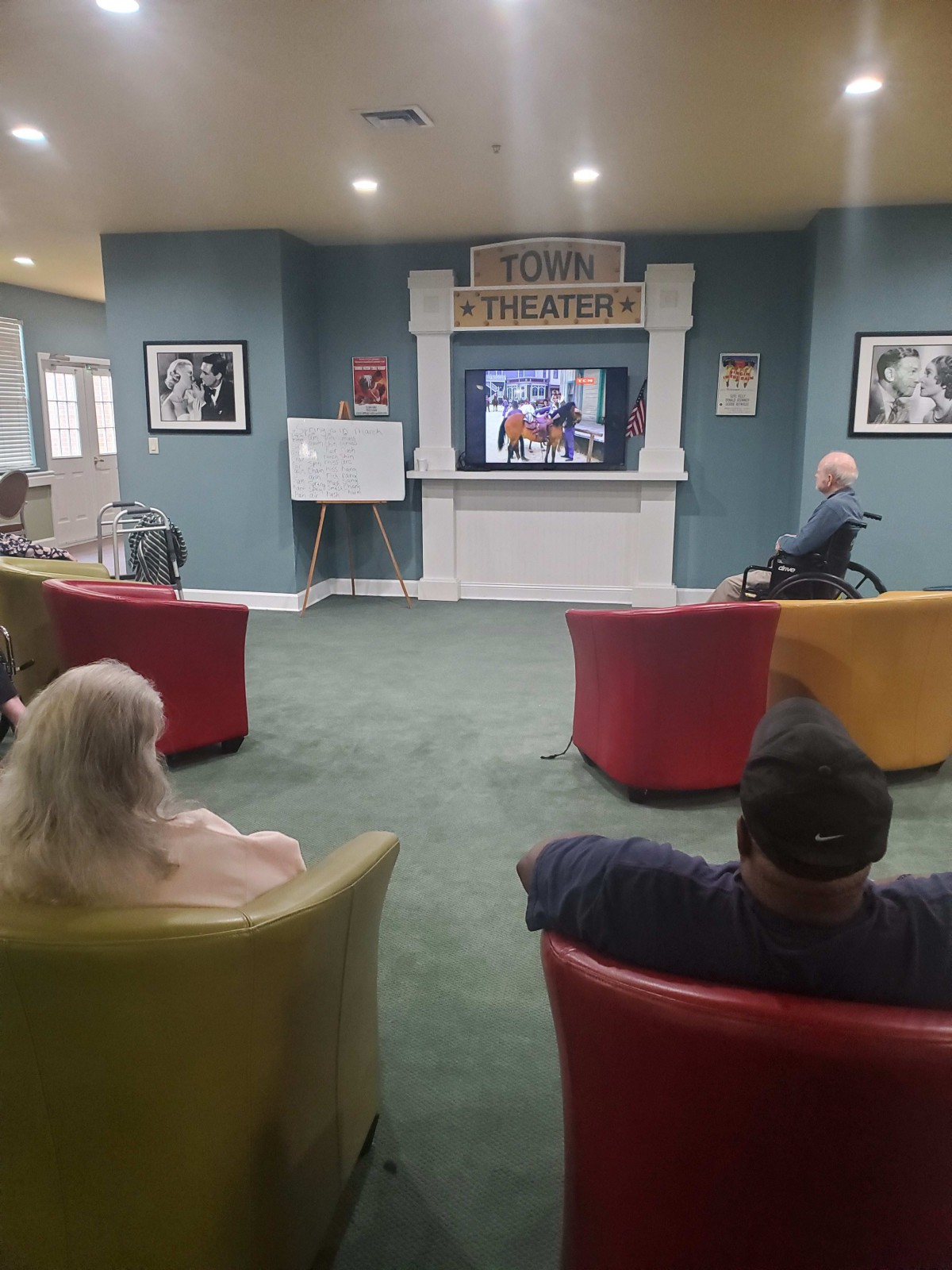 Residents gathered in a senior living community TV room, enjoying a show together.