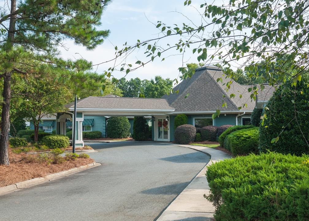 A quaint building with a circular driveway surrounded by trees and shrubs.
