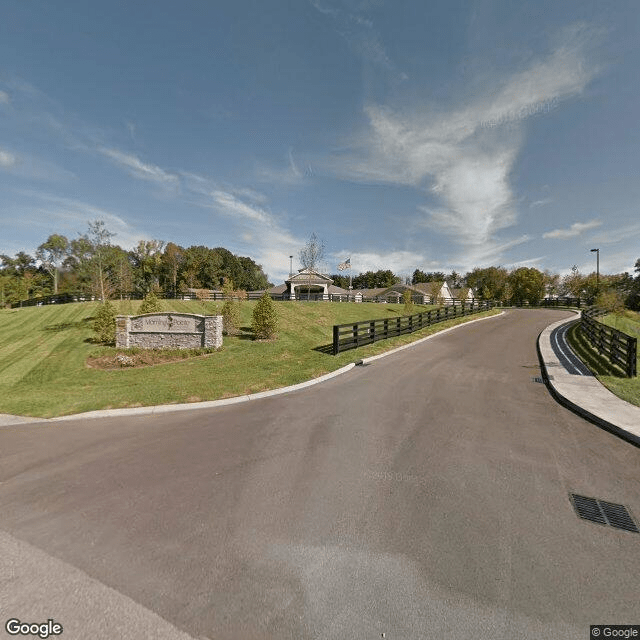 A road leading into a park with a visible sign and surrounding trees under a clear sky.