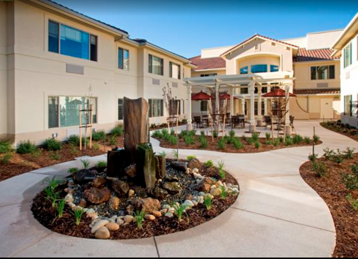 A courtyard featuring a central fountain surrounded by landscaping, adjacent to a large building with multiple floors.