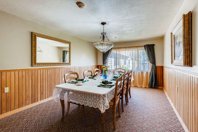 A well-decorated dining room with a large table set for a meal, featuring a chandelier and elegant curtains.