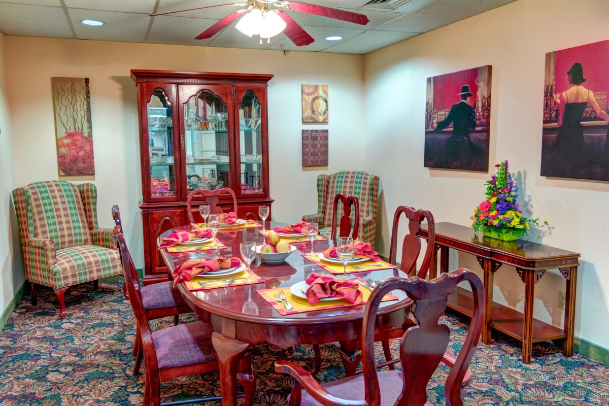 A traditional dining room featuring a polished wooden dining table with matching chairs, set for dinner. The room includes a china cabinet and wall art, creating a cozy atmosphere.