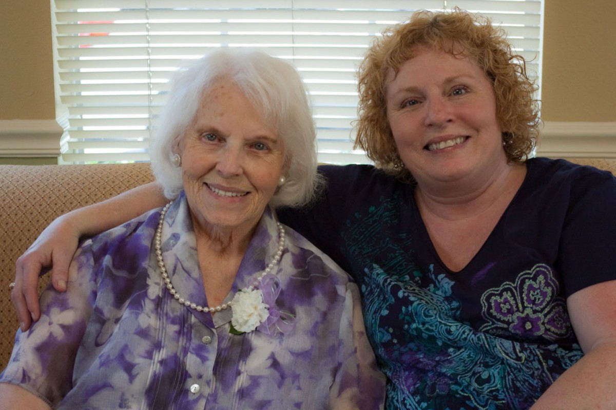 Two women smiling and sitting together indoors.