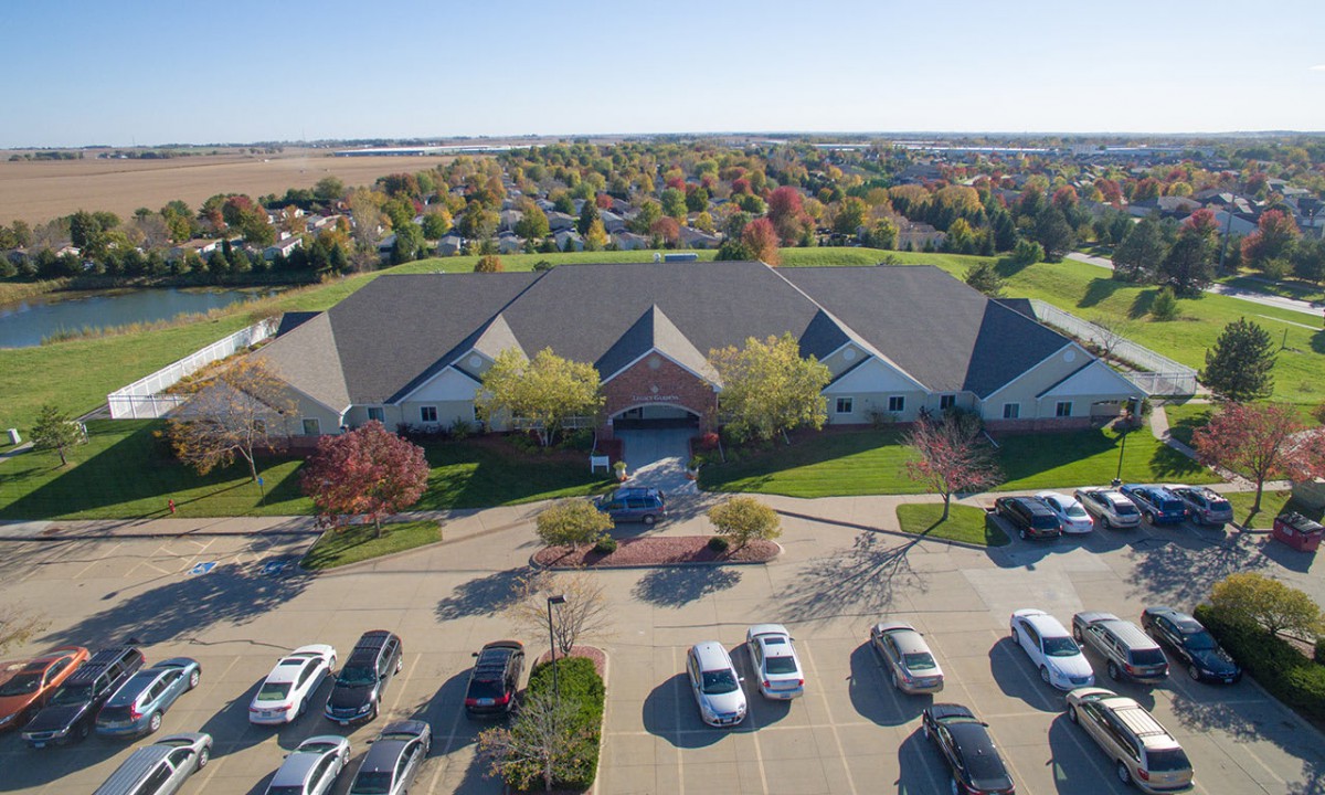 Aerial view of a suburban building with a parking lot surrounded by trees and a residential area in the background.