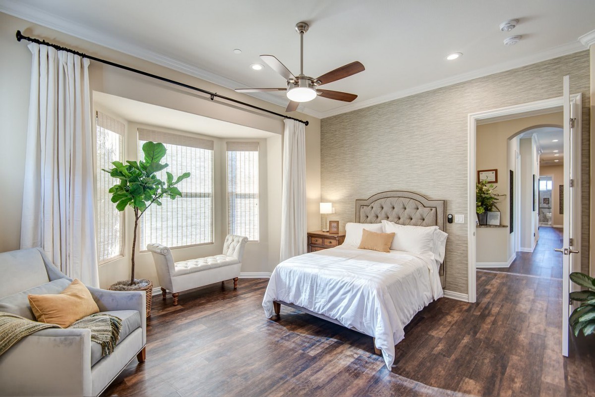 A modern bedroom with a cozy bed, hardwood floors, and ample natural light streaming through large windows.