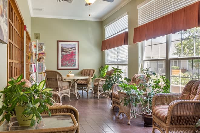 A cozy indoor seating area with wicker furniture and lush plants near large windows.