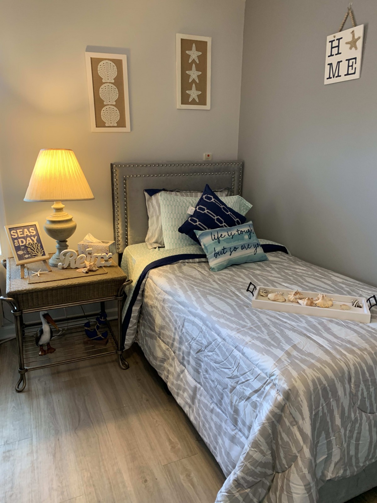 A cozy bedroom featuring a single bed with striped bedding, decorative pillows, and a lamp on a nightstand.