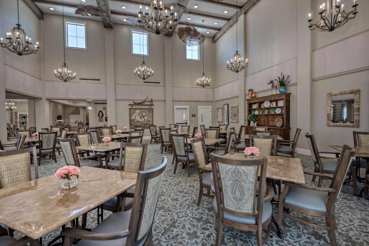 An elegant dining room with multiple tables and chairs, adorned with chandeliers and decorative elements.