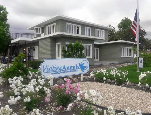A charming house with a welcoming sign, surrounded by beautiful flowers on a cloudy day.