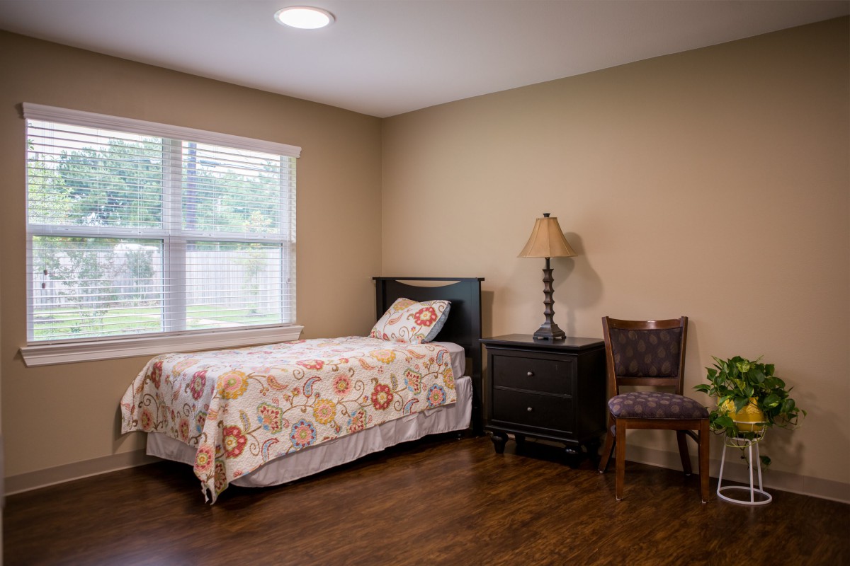 A cozy bedroom with a single bed, nightstand, and a chair by the window.