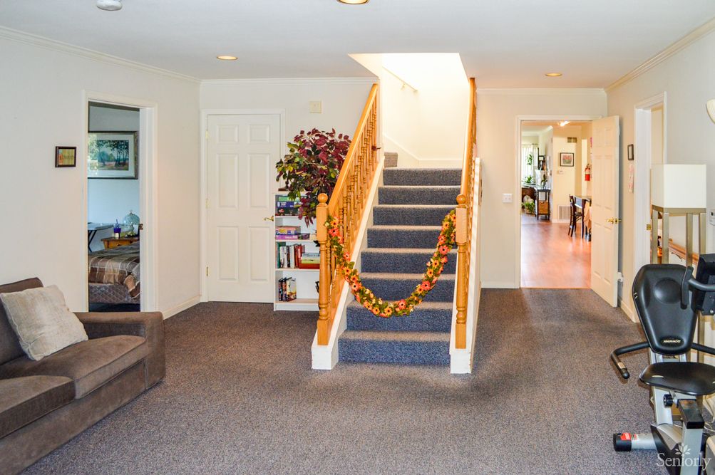 A cozy living room featuring a decorated staircase with garlands, carpeted flooring, and a bookcase next to the stairs.