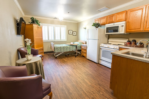 A spacious, well-lit room featuring a kitchen area and a hospital bed, designed for comfort and care.