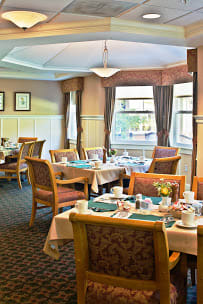 A cozy dining room with neatly arranged tables and chairs, featuring large windows with curtains.