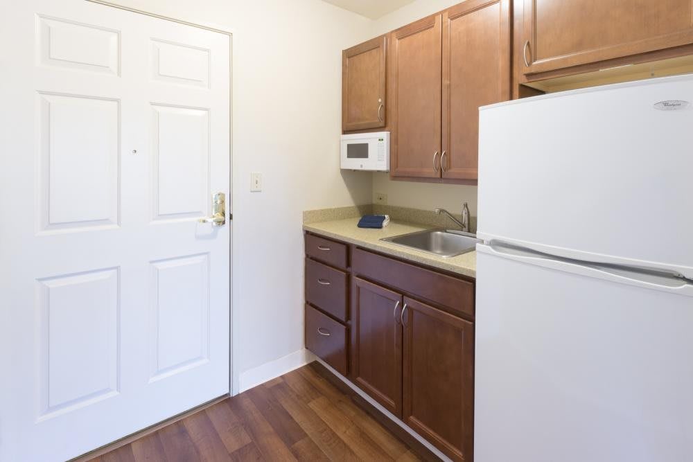 A compact kitchen with wooden cabinets, a sink, a refrigerator, and a microwave.