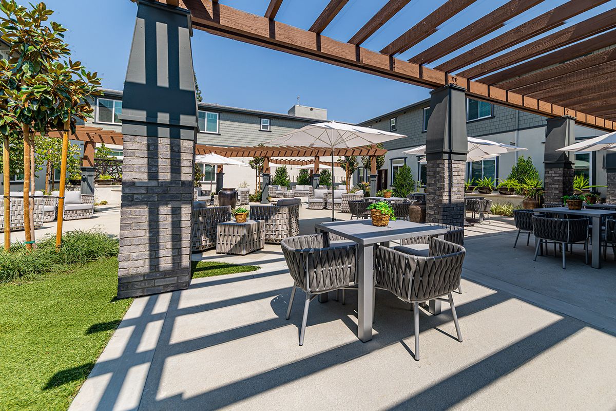A sunny outdoor patio with comfortable seating, shaded by a pergola.