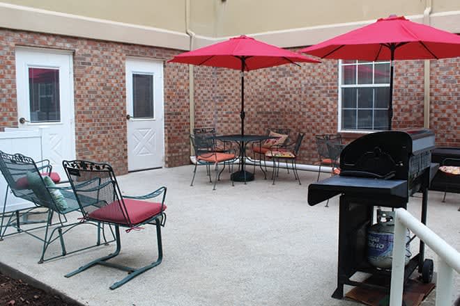 A cozy outdoor patio area with tables, chairs, and umbrellas next to a brick wall.