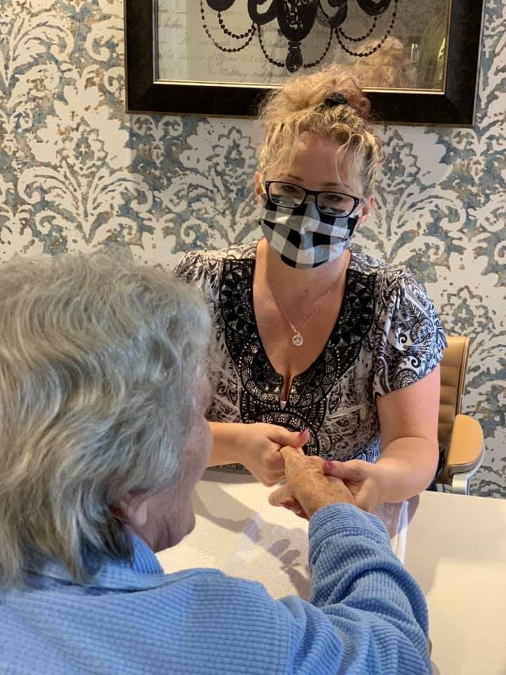 A person wearing a face mask provides a manicure to an elderly individual indoors.