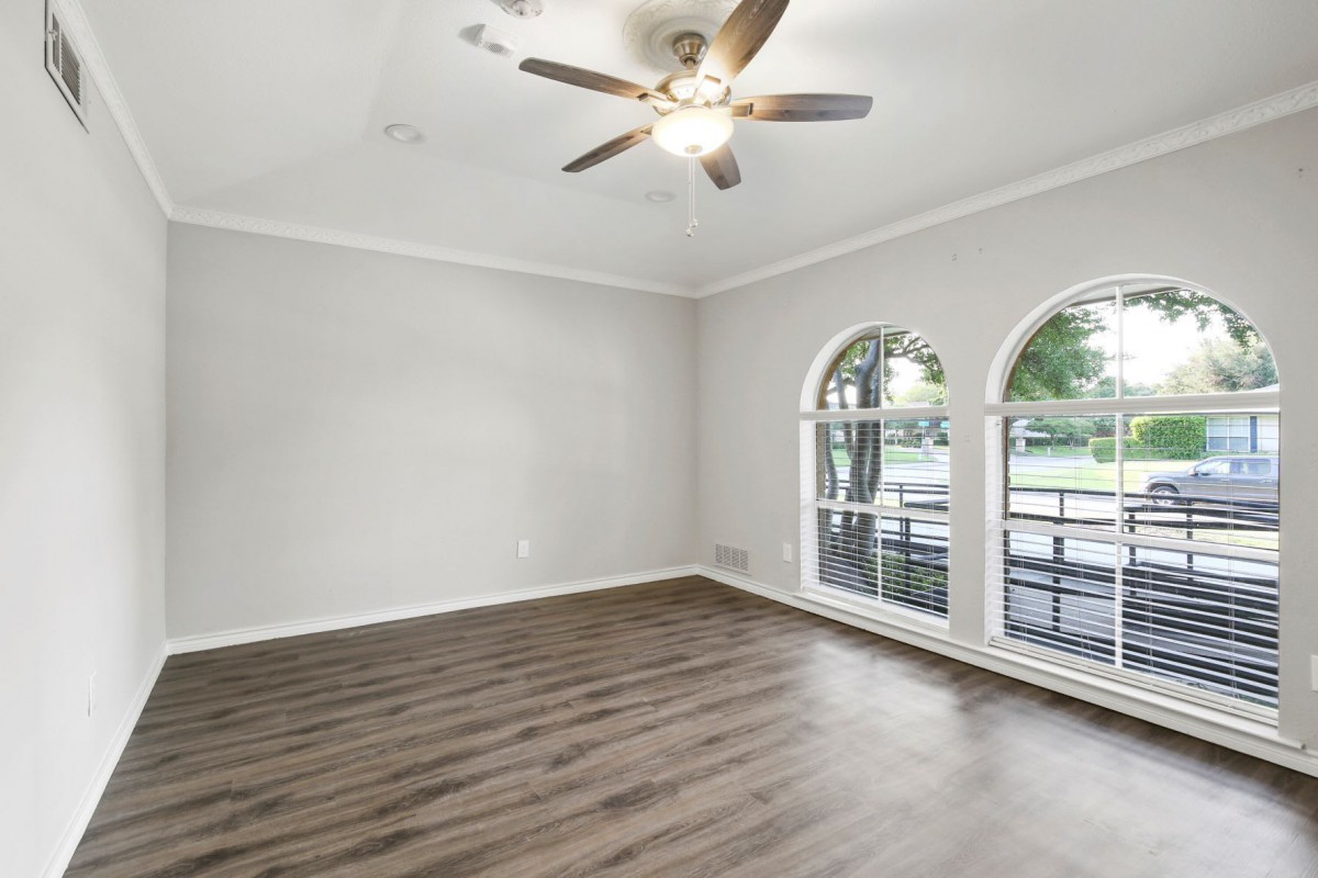 A modern living room with hardwood floors, large windows, and a ceiling fan.