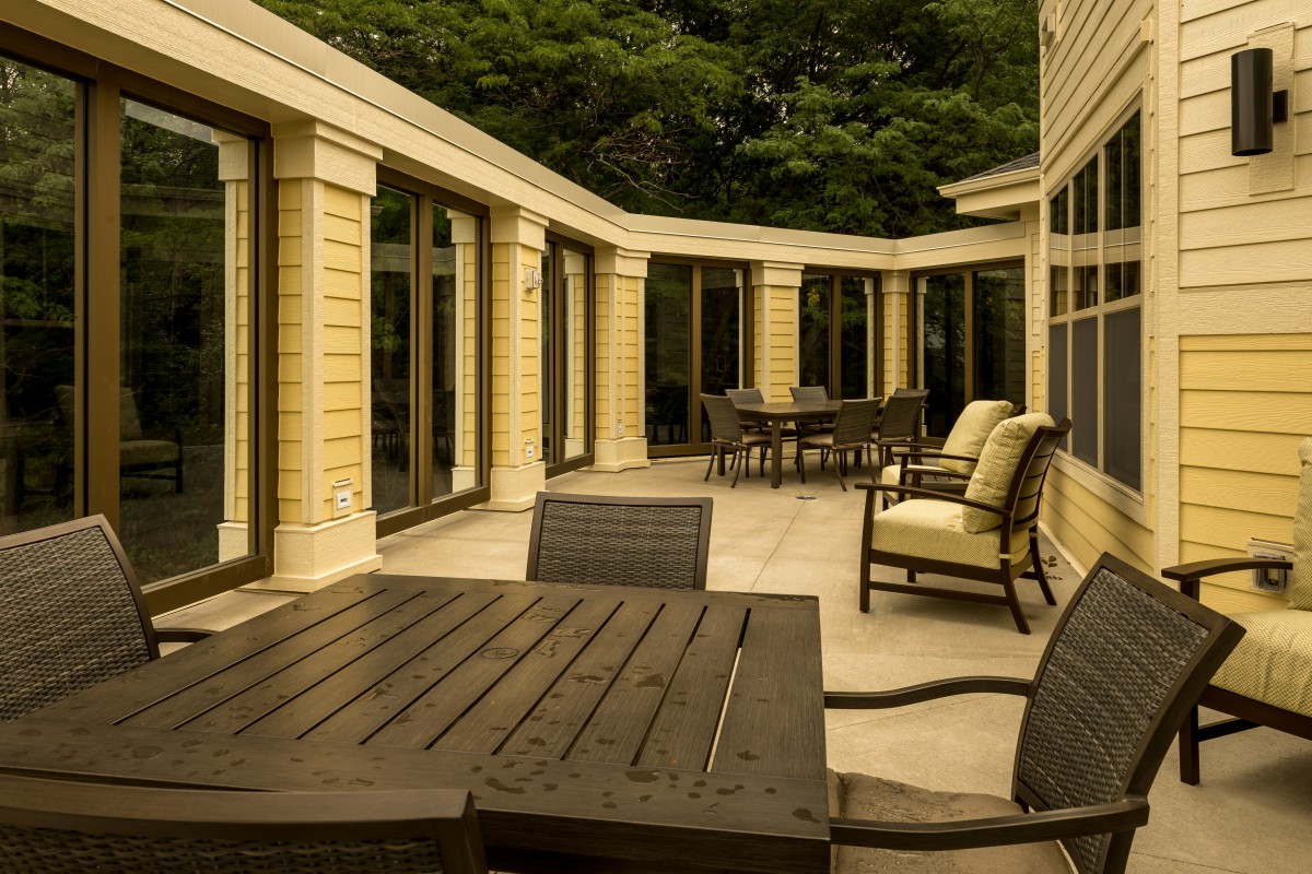 A spacious patio featuring outdoor furniture and surrounded by glass doors, with trees in the background.