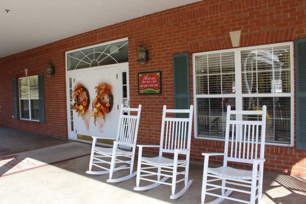 A cozy front porch adorned with white rocking chairs and festive wreaths on the entrance doors of a brick building.