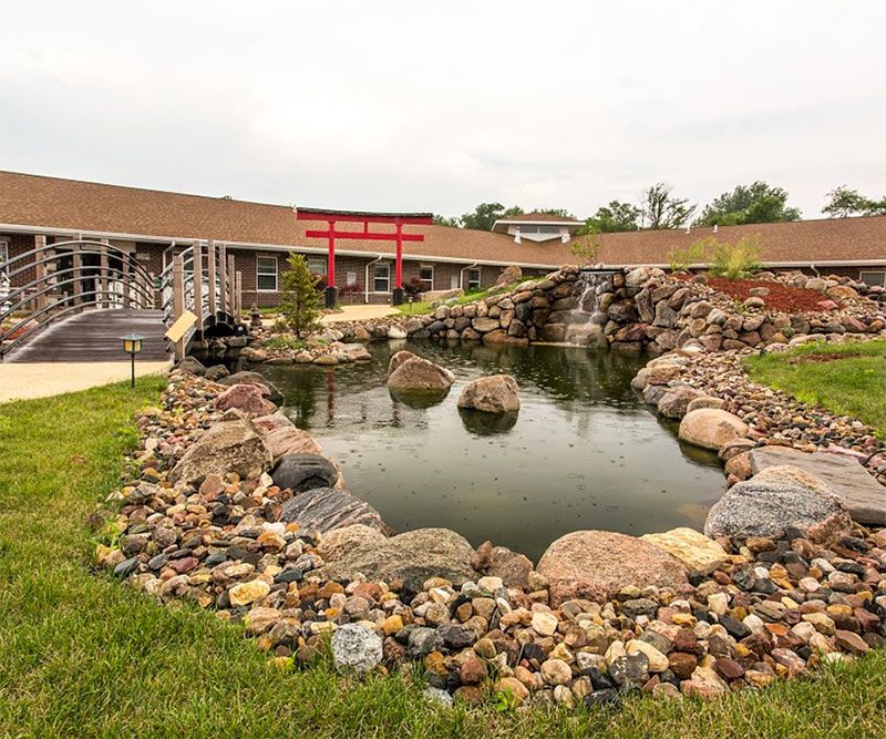 A landscaped area featuring a pond surrounded by rocks, adjacent to a building.
