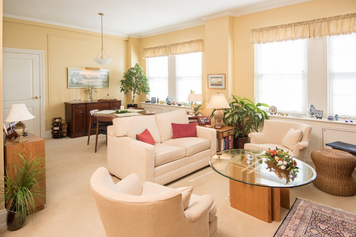 A cozy and well-decorated living room featuring comfortable seating, a glass coffee table, and lush plants.