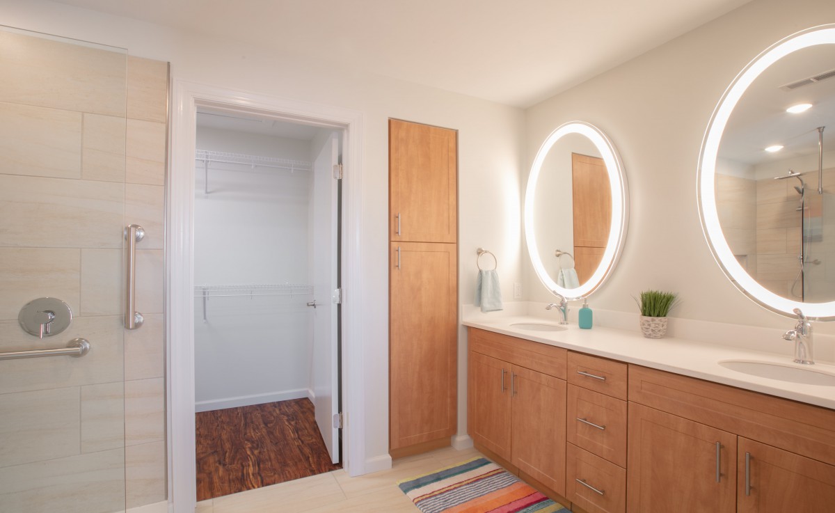 A modern minimalist bathroom with a lighted oval mirror and wooden cabinetry.