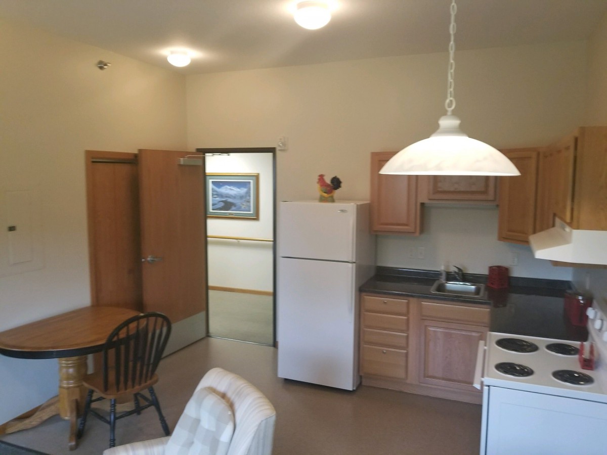A cozy apartment kitchen with wooden cabinets, a dining table, and a white refrigerator.