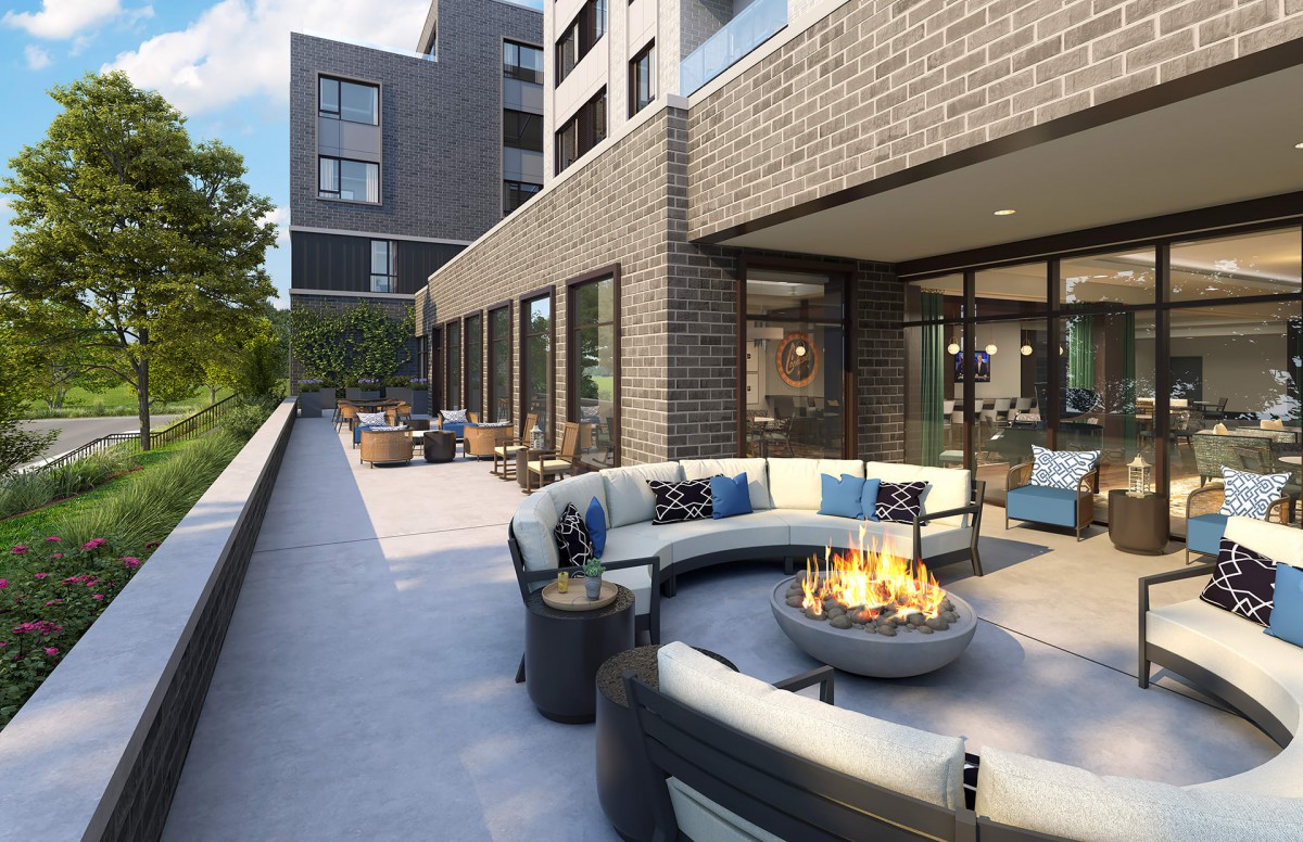 A modern outdoor terrace with a circular seating area and firepit, adjacent to an apartment building.