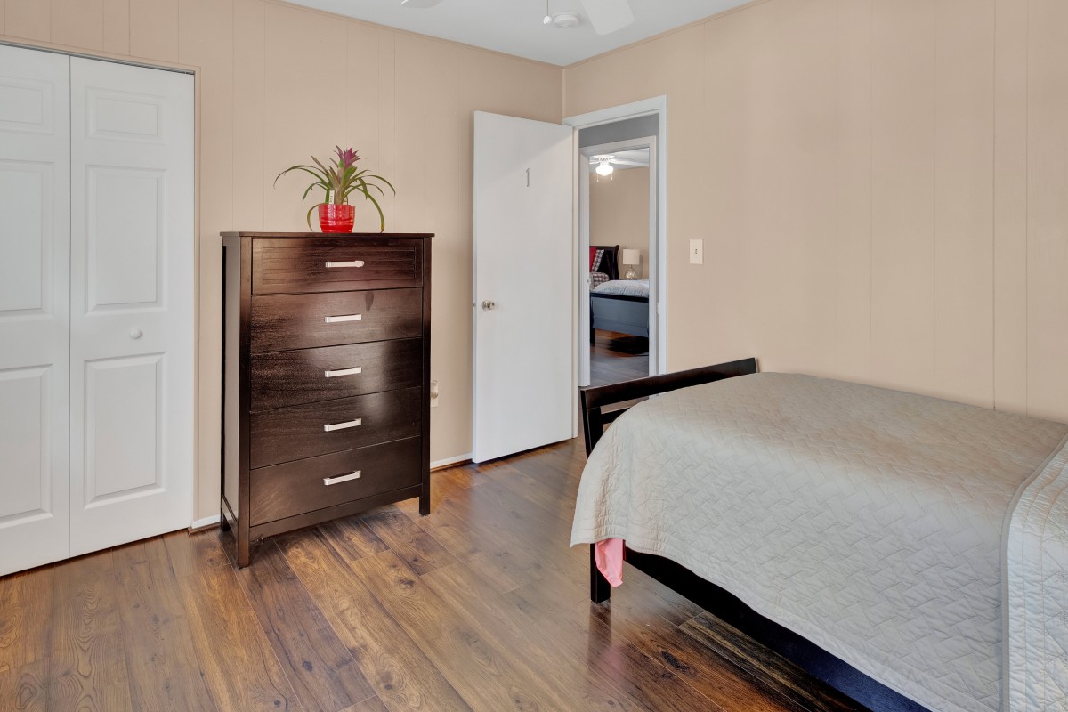 A neatly organized bedroom with a dark wooden dresser, a bed, and hardwood flooring.