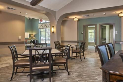 A well-lit dining area with wooden tables and chairs, featuring cozy lighting and large windows.