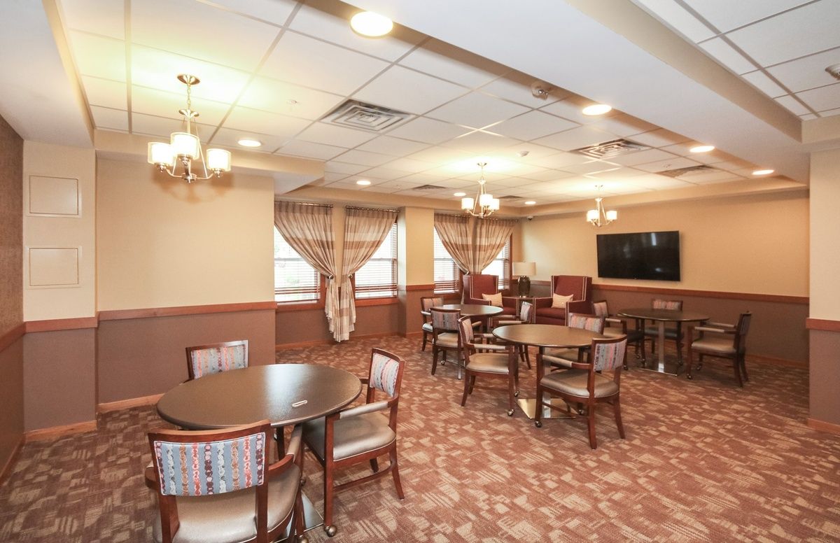 A cozy dining room with multiple tables and chairs, elegantly decorated with chandeliers and curtains, featuring a television on the wall.