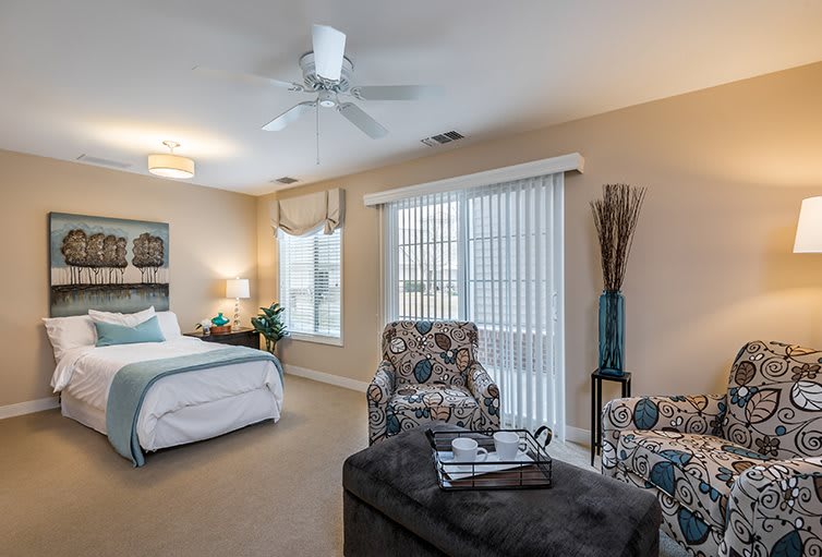 A cozy bedroom with stylish decor, featuring a bed, armchairs, and large windows.