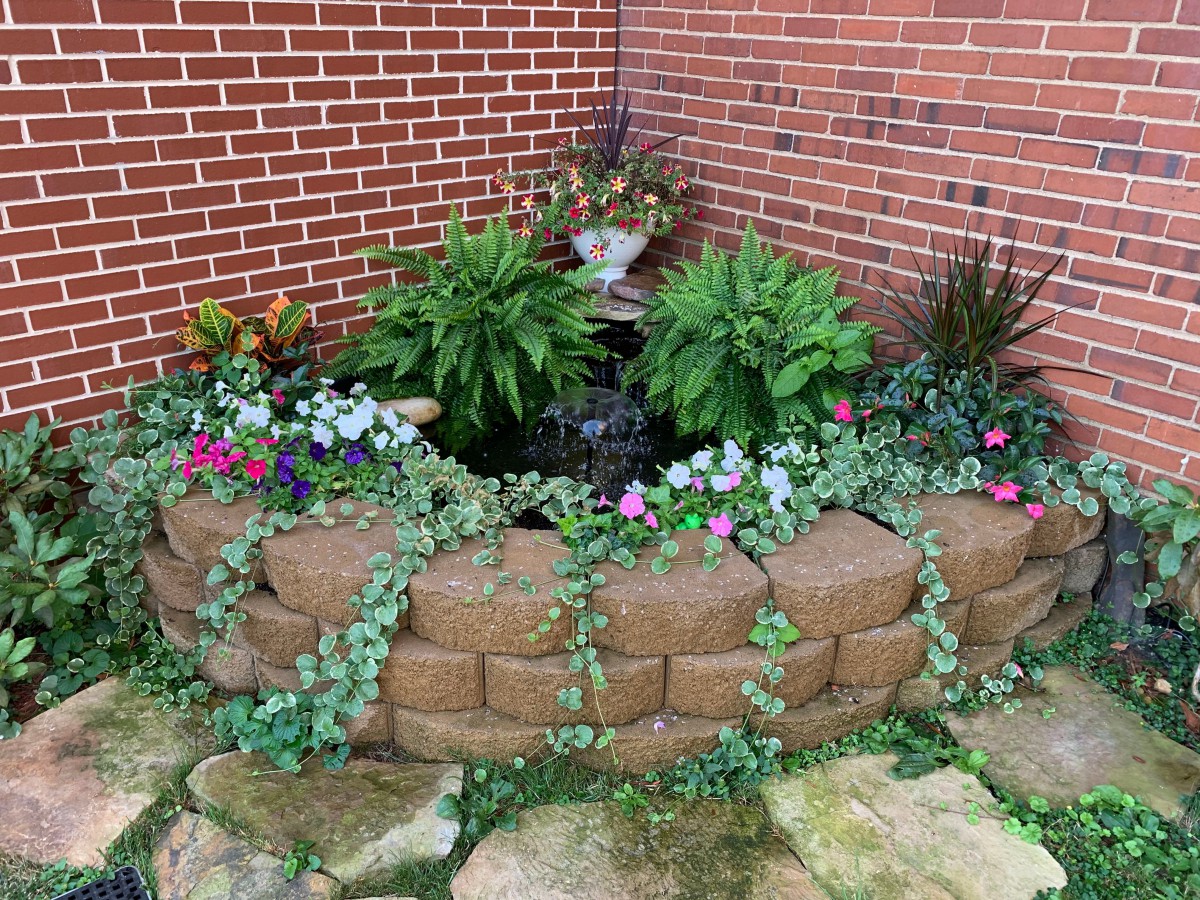A beautiful garden bed with various plants and flowers against a brick wall.