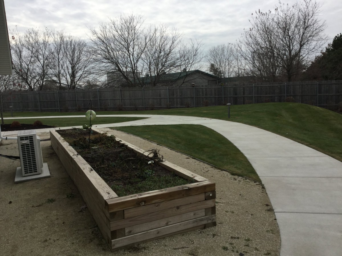 A wooden raised garden bed alongside a curved concrete pathway under an overcast sky.