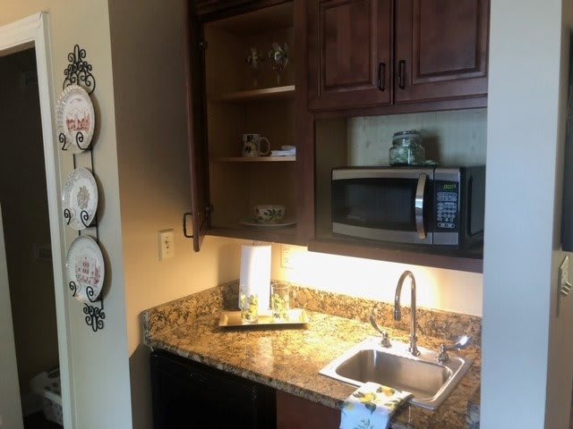 A small kitchen area with wooden cabinets, a granite countertop, a sink, and a microwave.