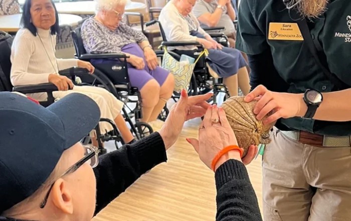 A group of elderly individuals engaged in a hands-on activity involving rope, with some seated in wheelchairs.