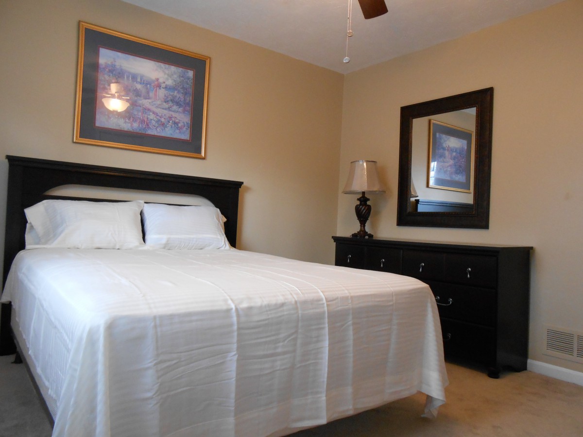 A neatly arranged bedroom with a bed, dresser, and mirror.