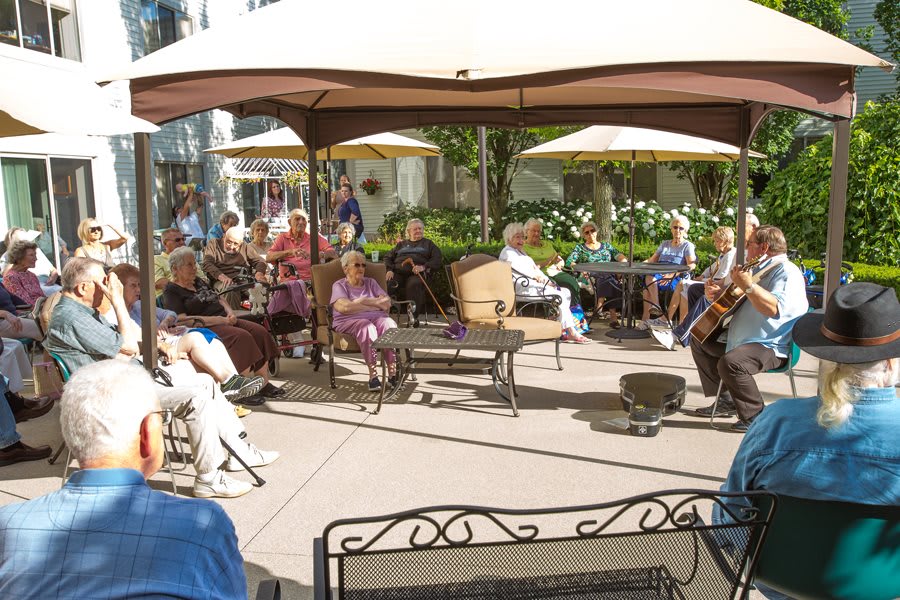 A group of seniors socializing in an outdoor patio area under canopies.