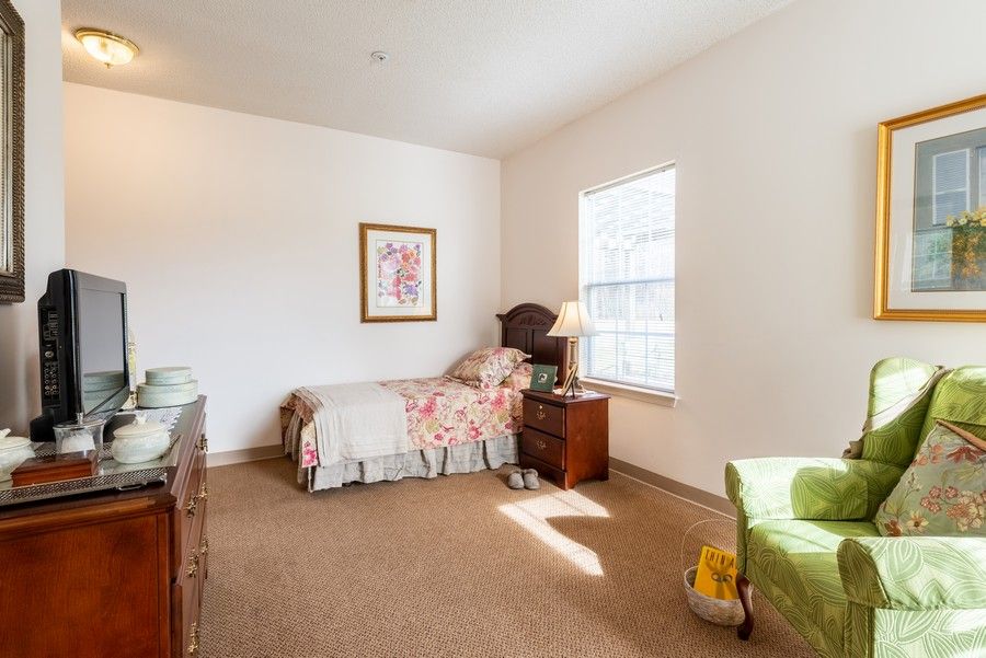 A cozy bedroom with a single bed, wooden furniture, and a large window letting in natural light.
