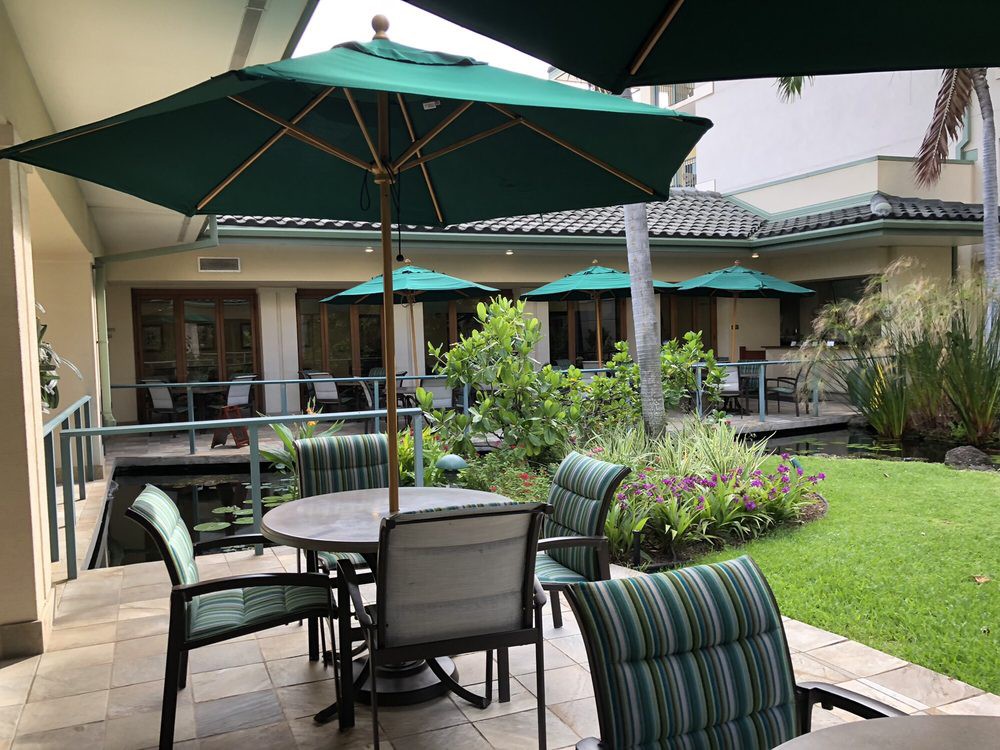 Outdoor patio area with tables, chairs, and green umbrellas surrounded by lush garden.